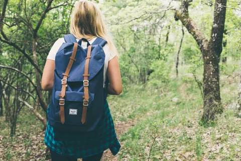 Senderista con mochila caminando por sendero entre vegetación frondosa