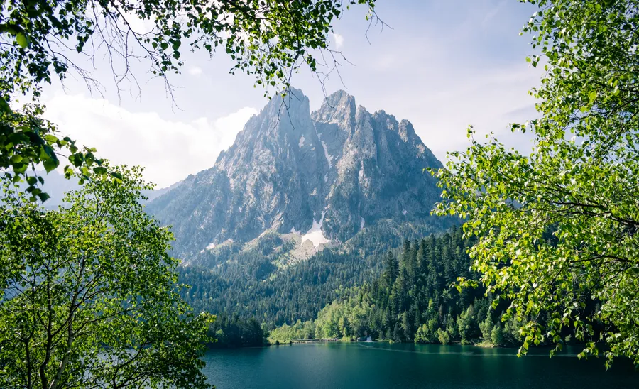 Els Encantats sobre el Estany de Sant Maurici entre el arbolado de la orilla, Parc Nacional d'Aigüestortes